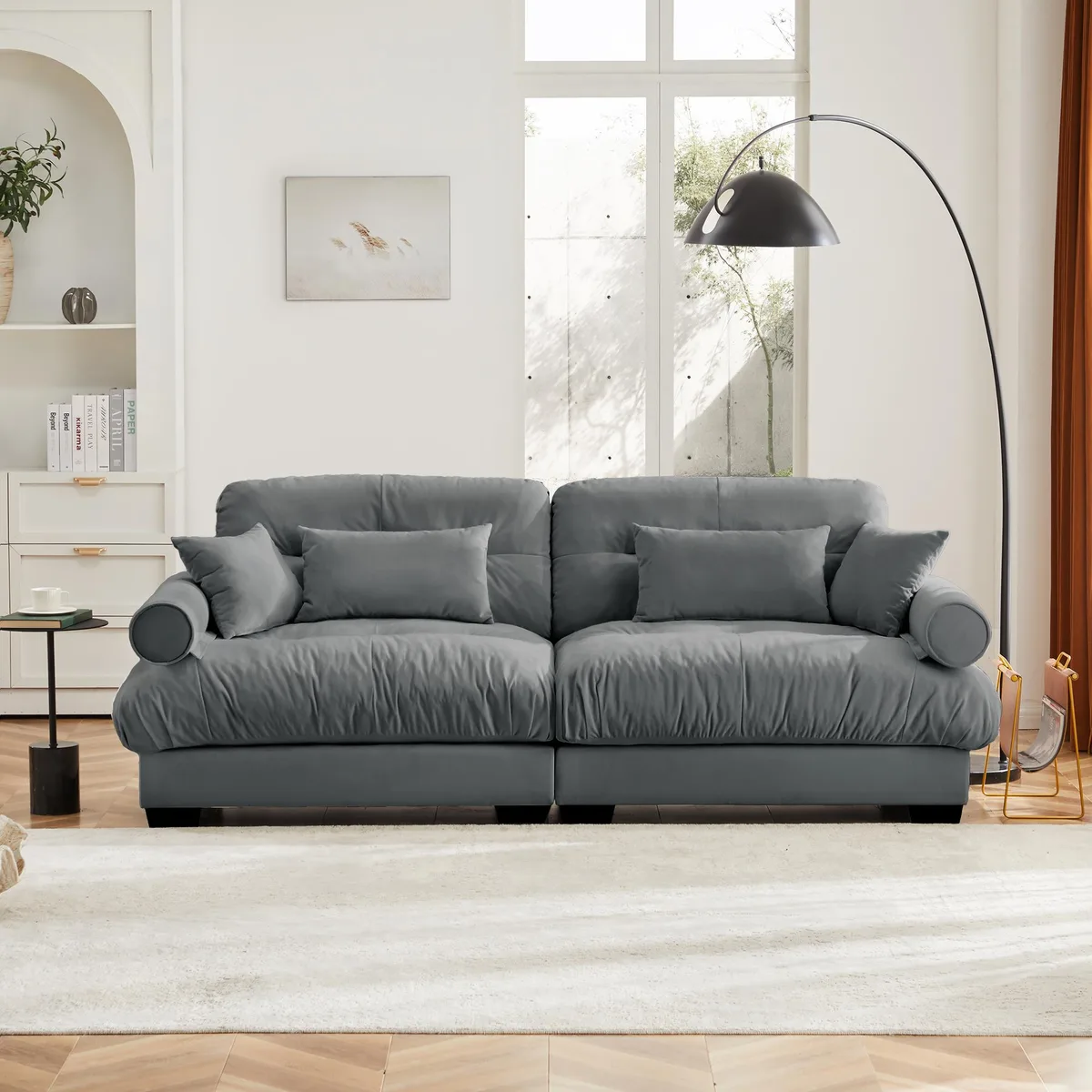 Grey velvet two-seater sofa with rounded bolster armrests and matching throw pillows