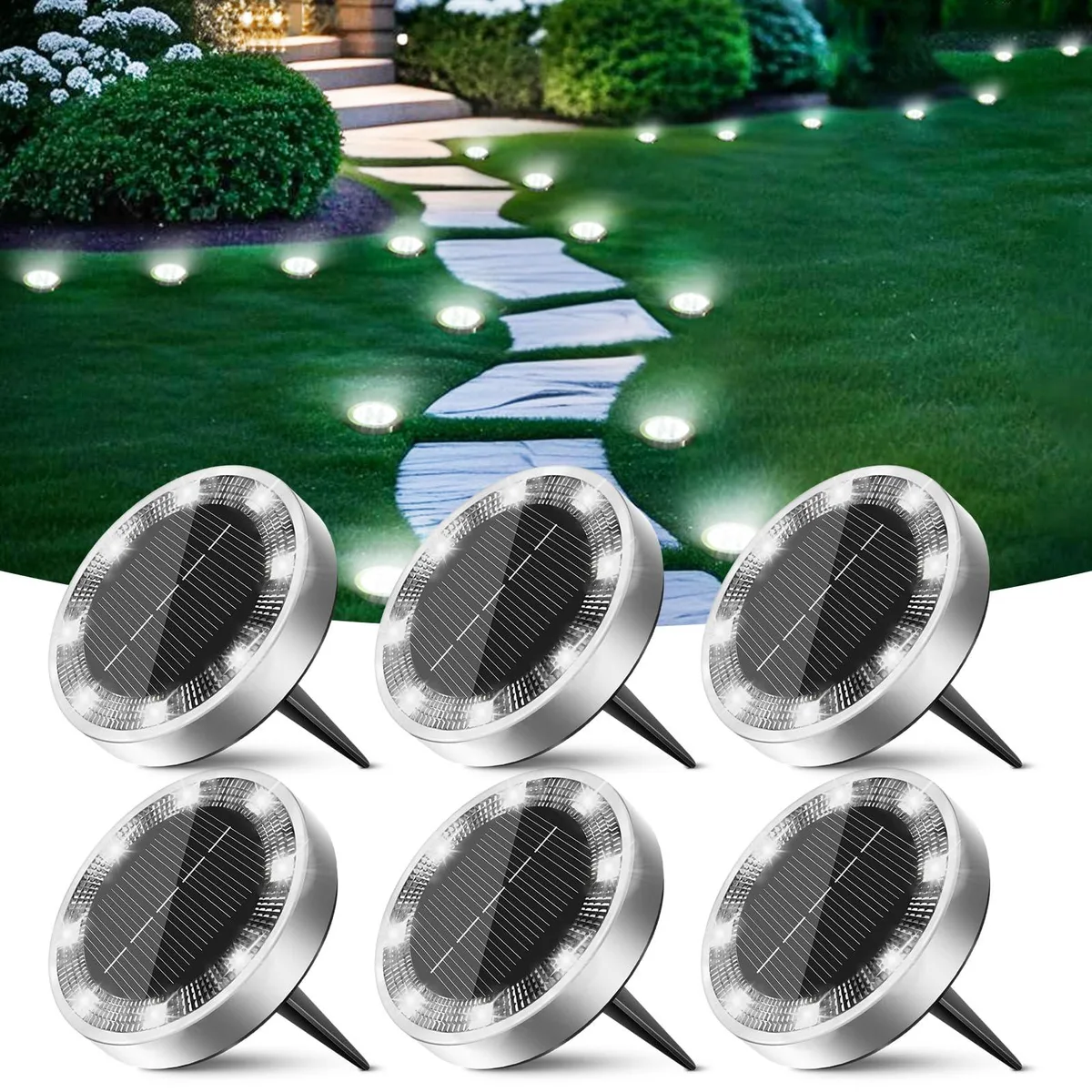 Six flat white solar discs with plastic lenses and stainless steel spikes lie on grass
