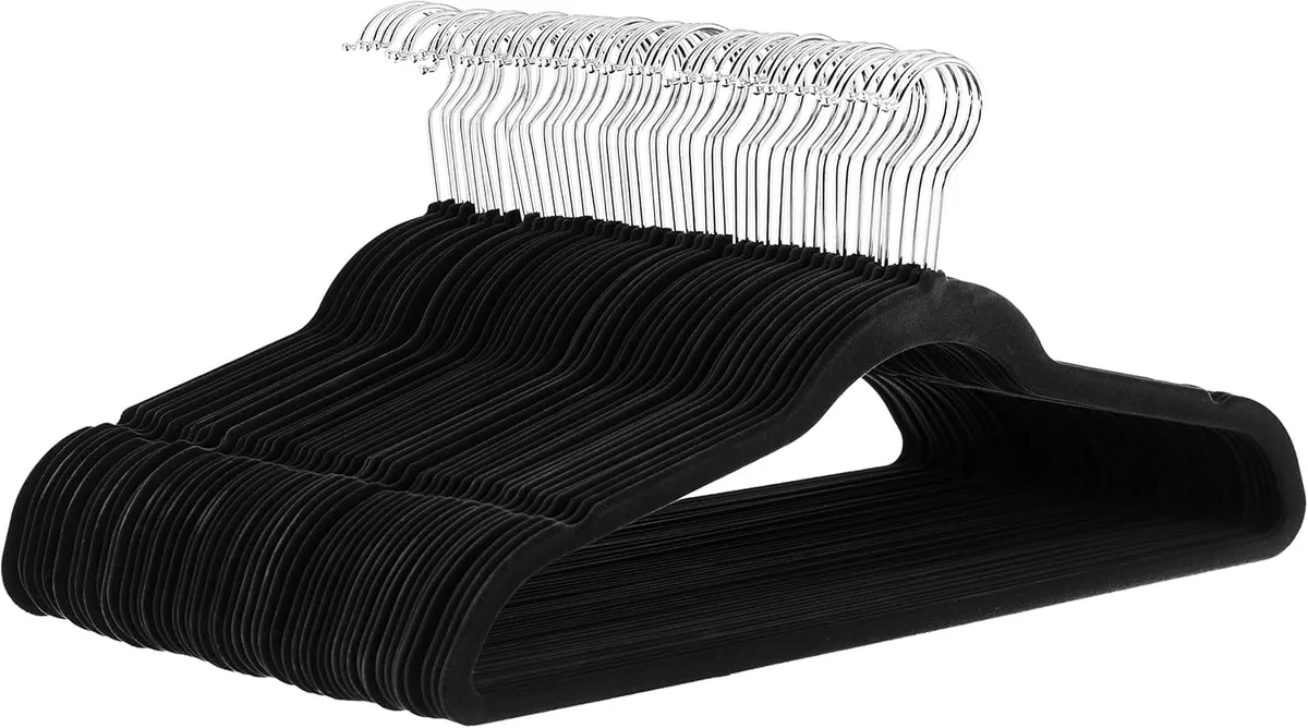 Thirty slim black and silver velvet hangers with notched shoulders on a light background