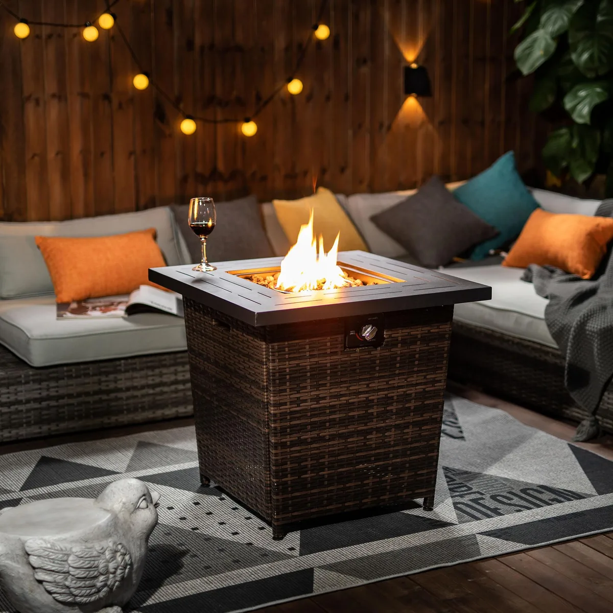 Square 28 inch black steel fire table with brown wicker base and decorative stones