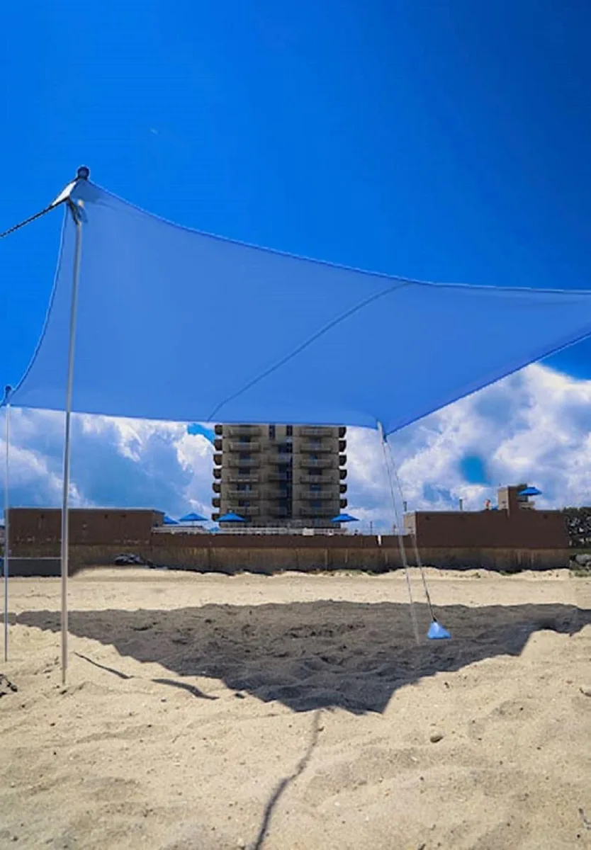 Royal blue pop-up canopy shade with four poles and sandbags on beach sand