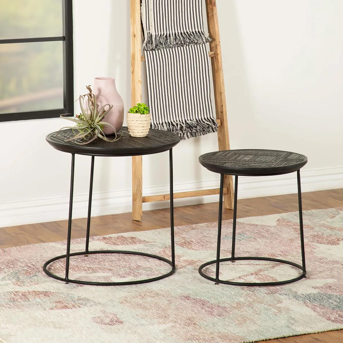 Two matte black metal-framed nesting tables with mango wood tops, one sliding under the other