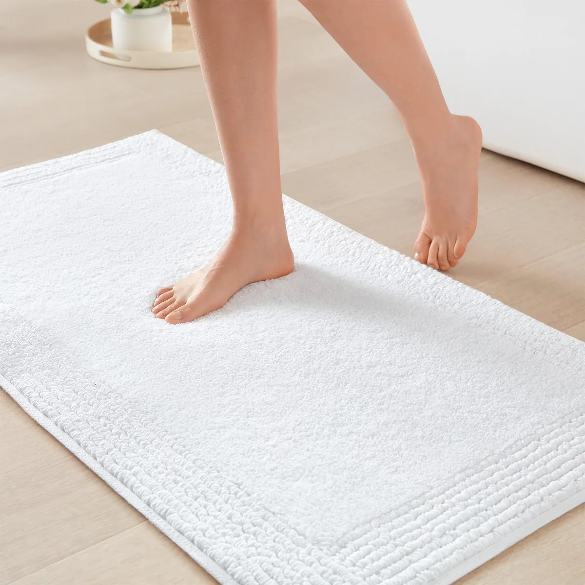 Rectangular white cotton bath rug with plush tufted surface, 21 by 34 inches