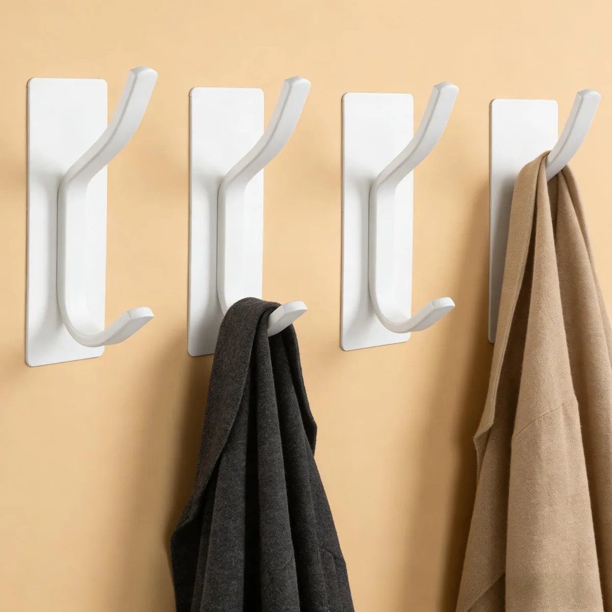 Four white stainless steel adhesive wall hooks with rounded pegs and flat rectangular bases