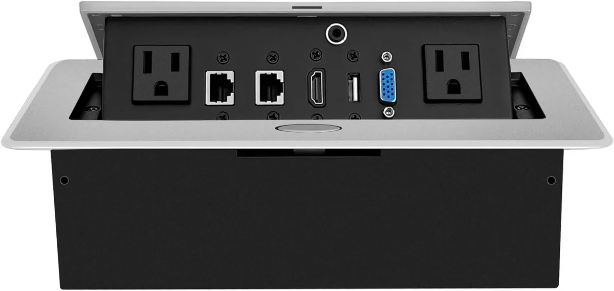 Silver rectangular pop-up box with brushed aluminium lid showing US power outlets, RJ45, HDMI, USB, VGA and 3.5 mm ports