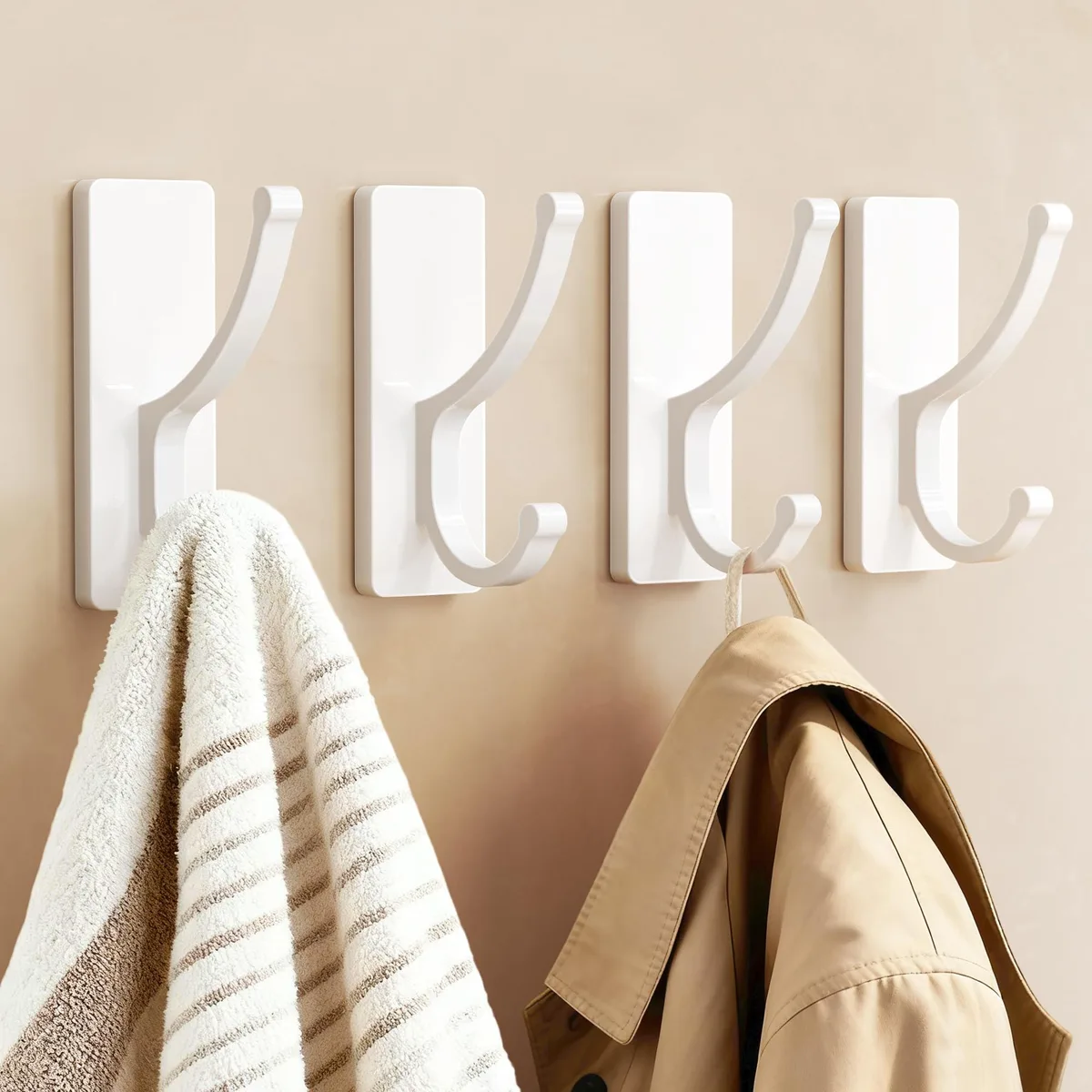 Four white adhesive wall hooks with strips on a surface