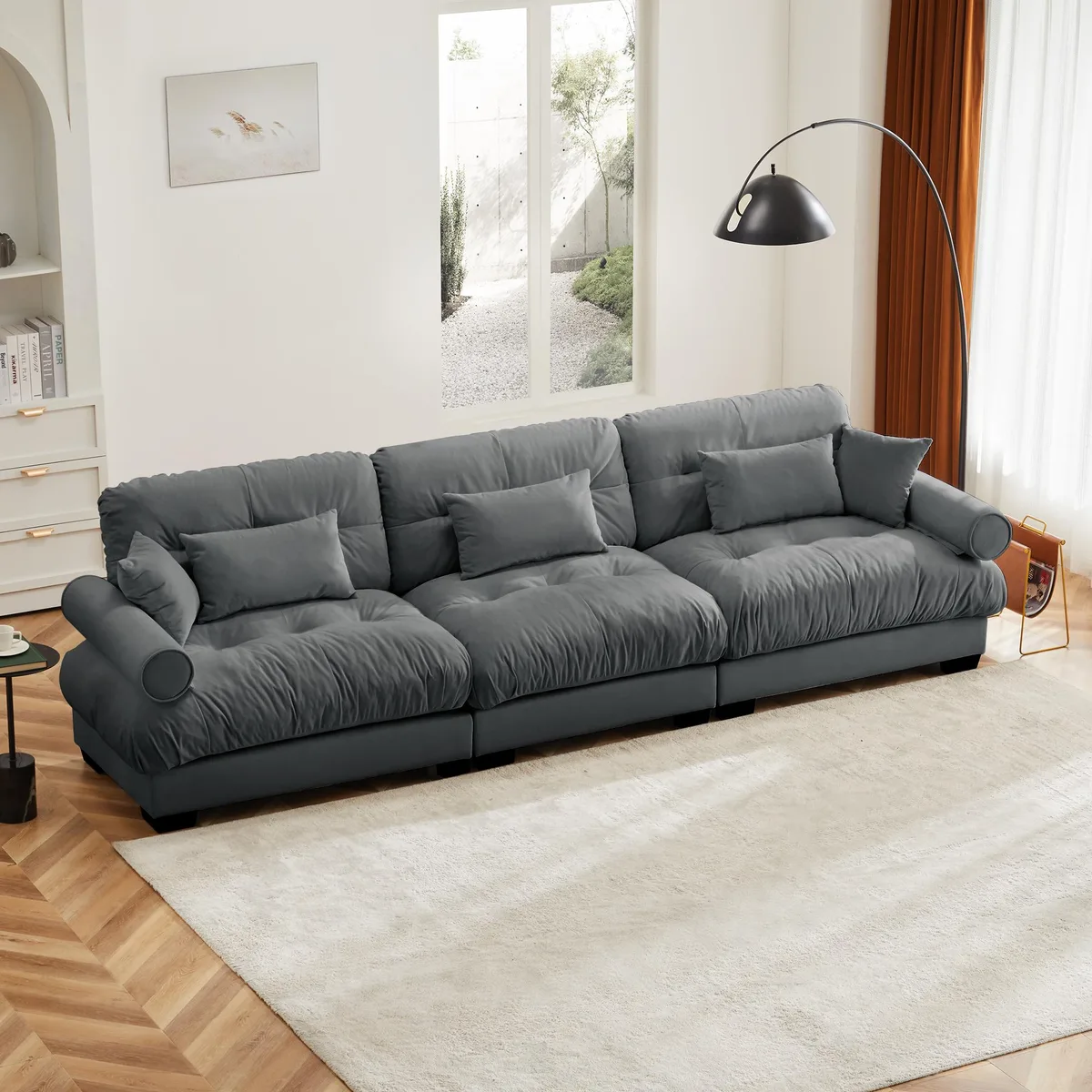 Large grey velvet three-seater sofa with round bolster arms and matching pillows