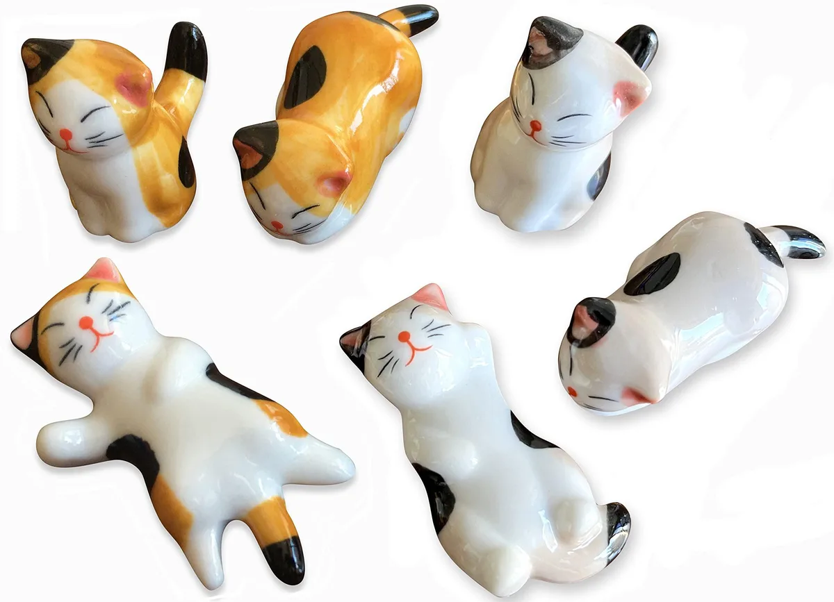 Sixteen small ceramic cat chopstick rests in varied poses with floral pattern finish