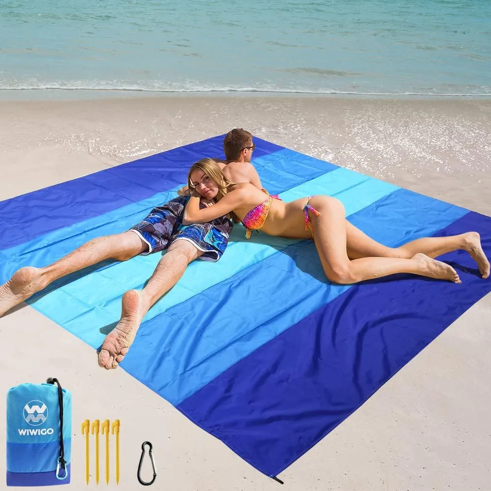 Navy blue rectangular beach blanket folded inside carry bag with stakes and carabiner