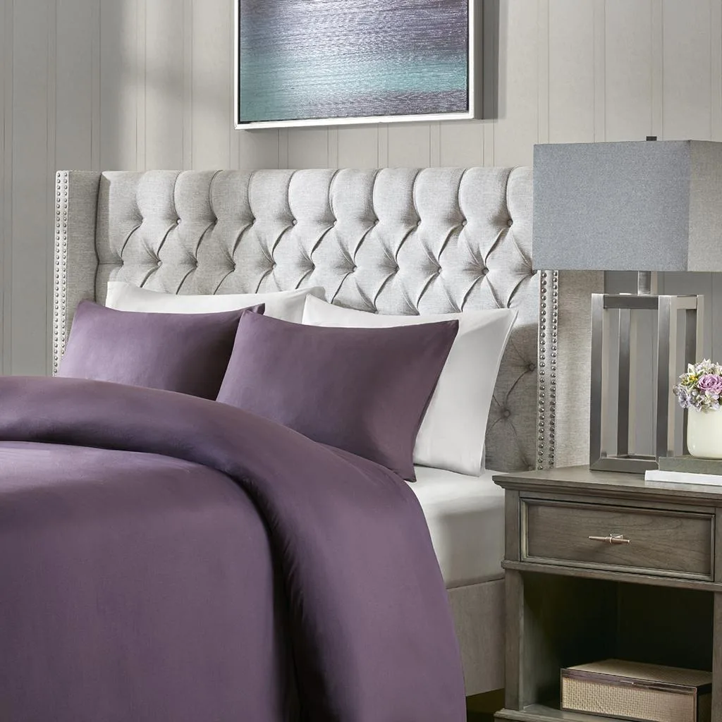Grey upholstered queen headboard with button tufting and nailhead trim on wings, adjustable black metal legs visible at base