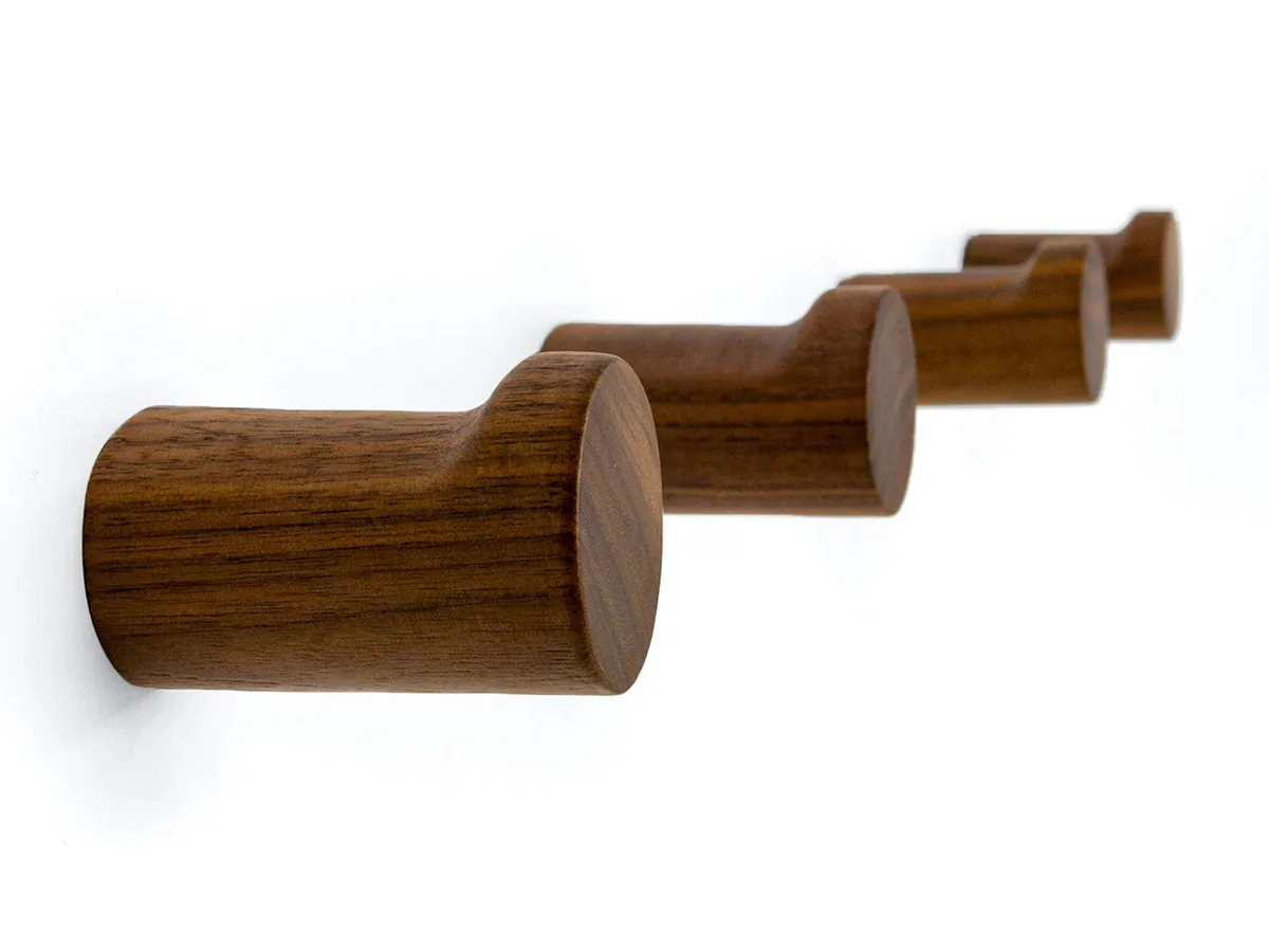 Four black walnut L-shaped wooden wall hooks on a light surface
