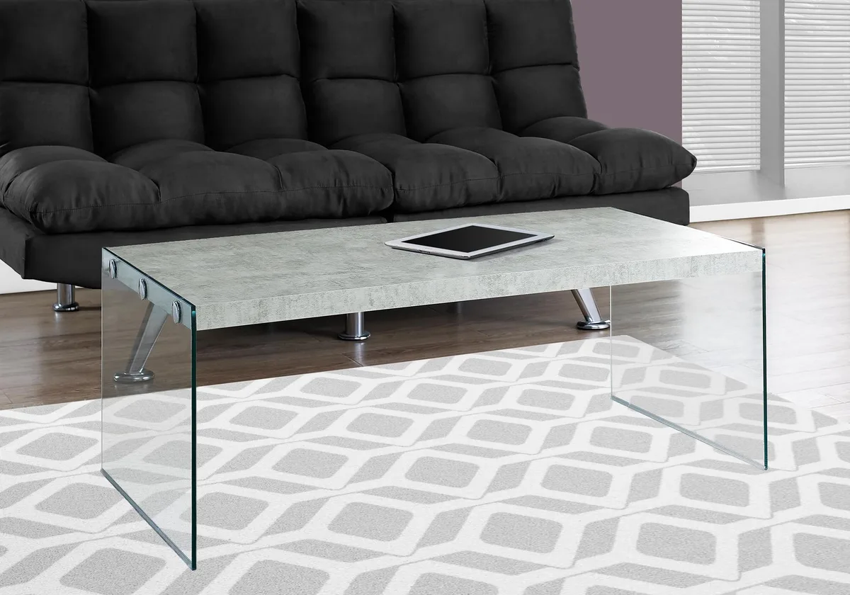 Grey rectangular coffee table with cement-look top and clear glass sides, 44 by 22 by 16 inches