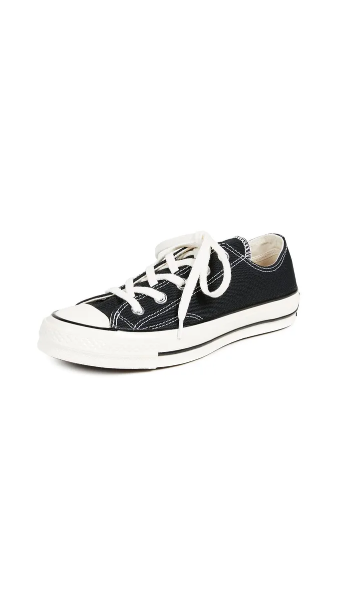 Black canvas low-top sneakers with white rubber toe cap and sole, contrast stitching, rounded toe, flat profile