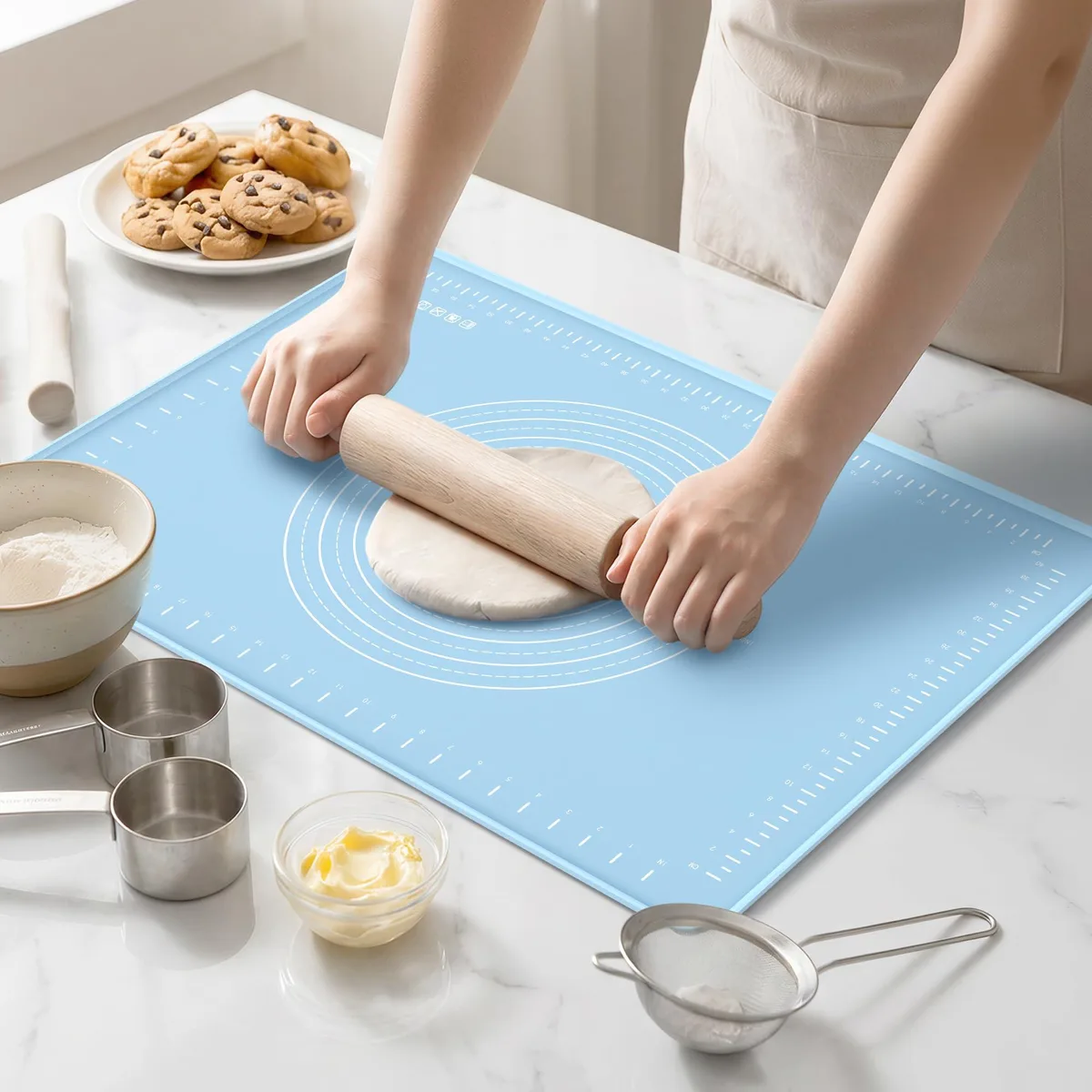 Rectangular blue silicone baking mat with printed measurements and raised edge, rolled and secured with a petal-shaped tie