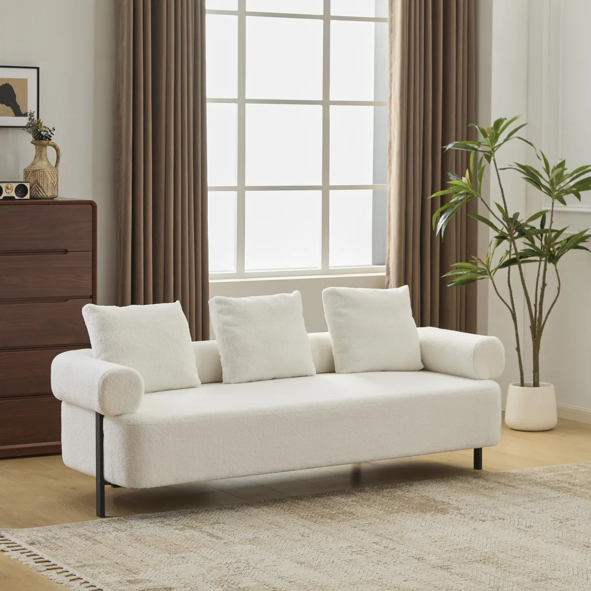 Beige boucle three-seater sofa with rolled arms, three plush pillows, and metal legs