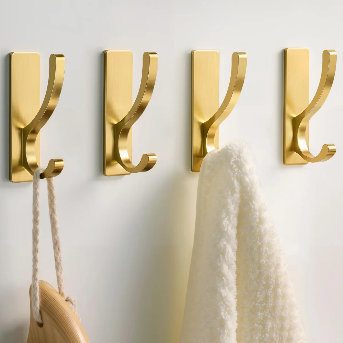 Four gold brushed metal adhesive hooks on a white background
