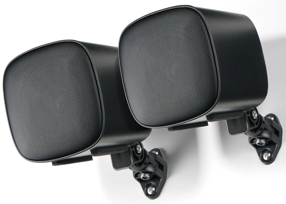 Pair of compact black passive bookshelf speakers with wall-mount brackets and bass port bungs