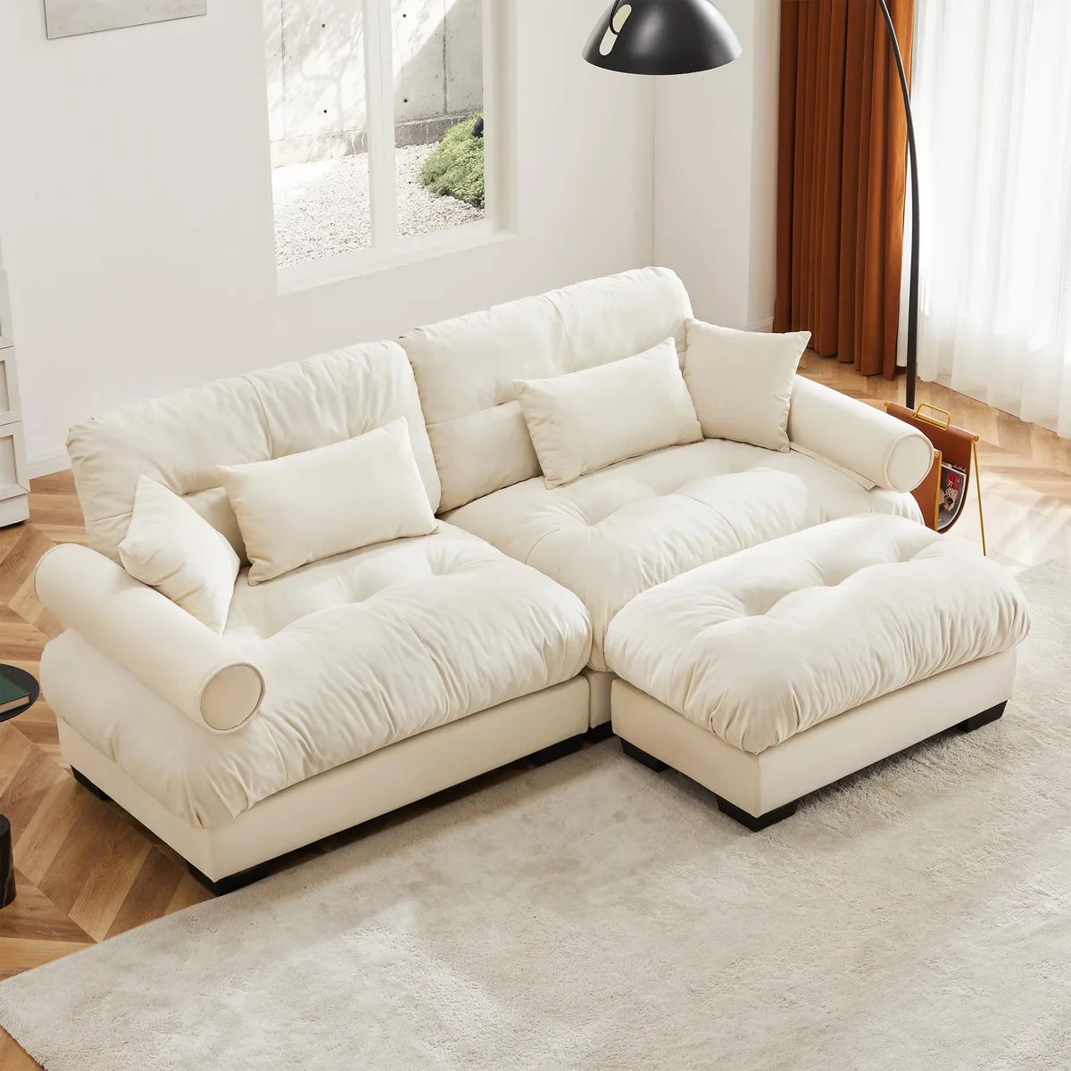 Cream velvet two-seater sofa with matching ottoman, round bolster armrests and scatter cushions