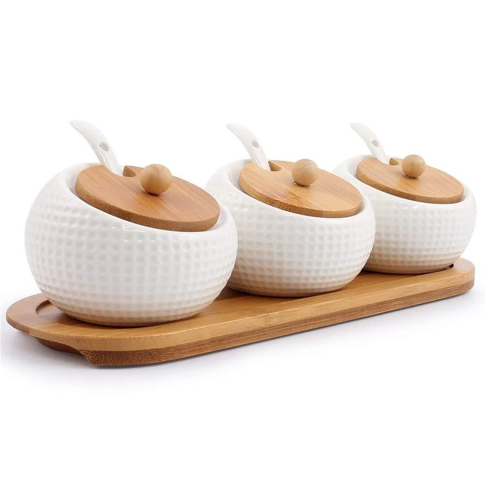 Three white porcelain jars with bamboo lids, ceramic spoons, wooden tray