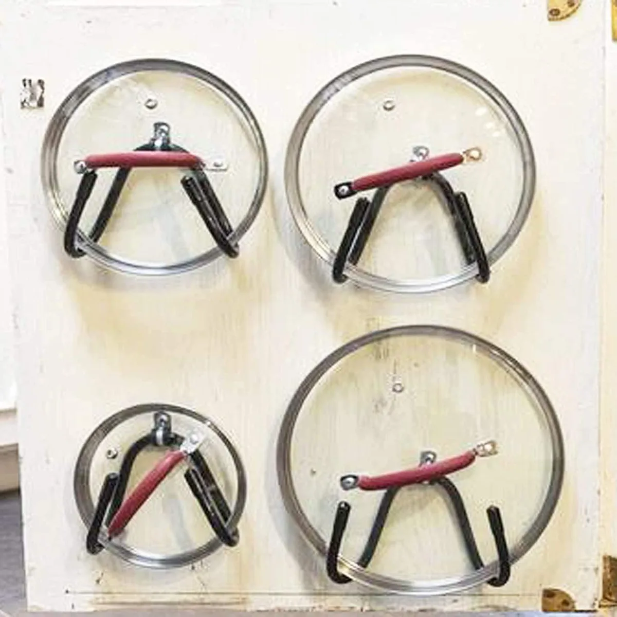 Four red metal pot lid brackets with adjustable rubber coated arms door mounted on cabinet interior