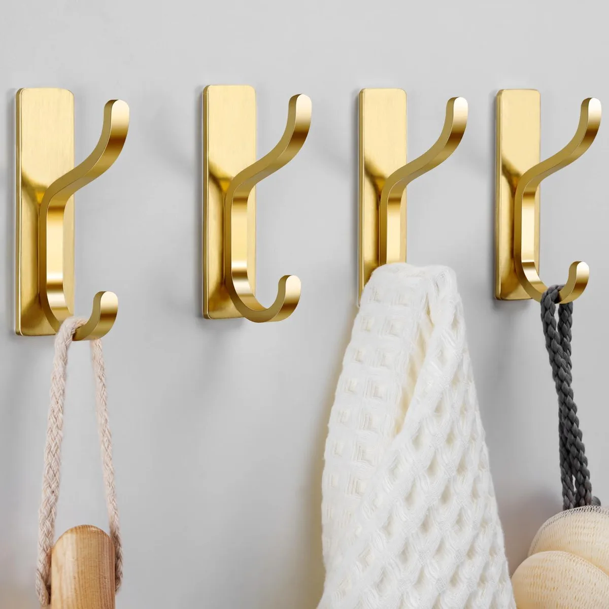 Four gold metal adhesive wall hooks on a surface