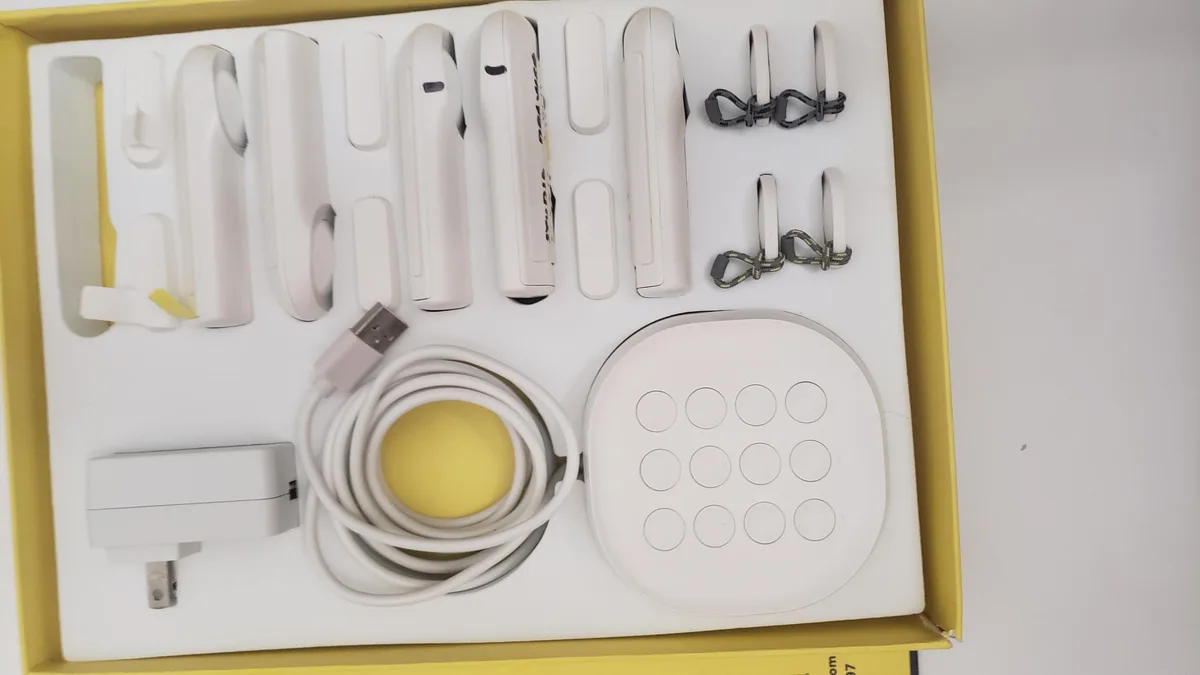 A white keypad hub and six small white motion and entry sensors on a plain surface