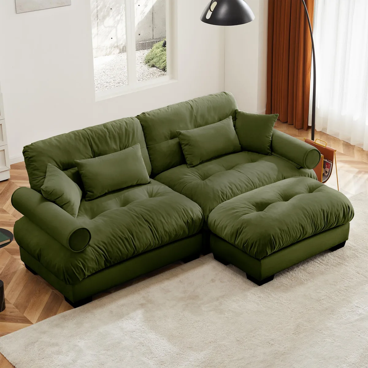 Olive green velvet two-seater sofa with matching ottoman, round bolster armrests, and scatter cushions