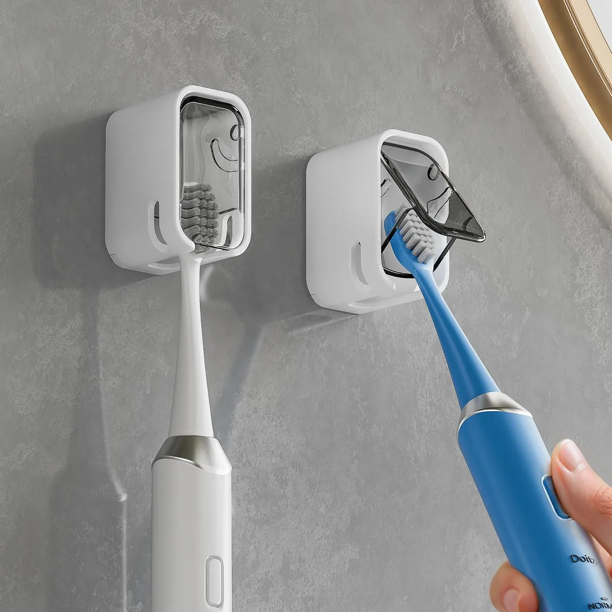 Two grey smooth plastic wall mounted toothbrush holders with covers, small rectangular form