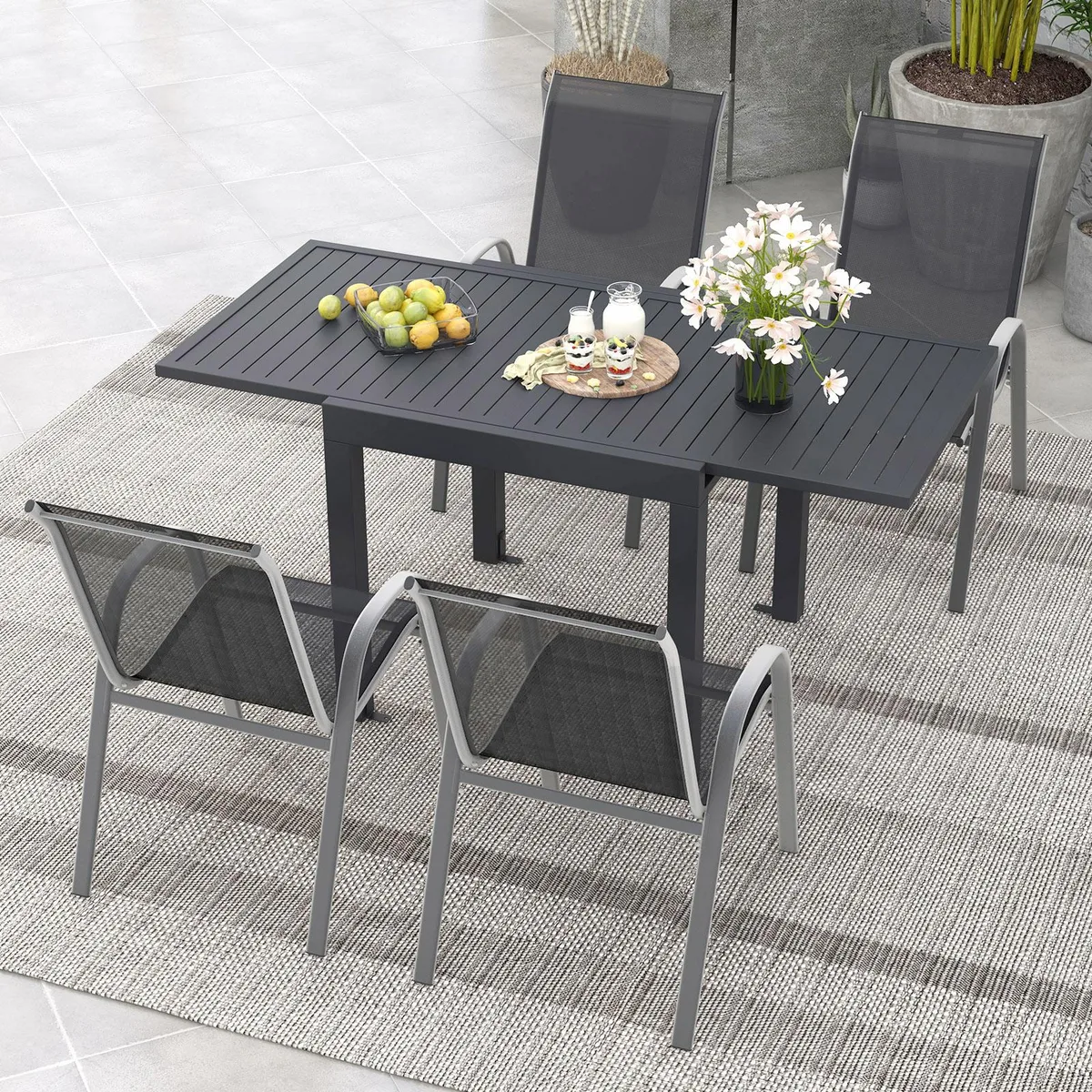 Dark grey extendable aluminum table with four black stackable chairs, tilted backrests and curved armrests