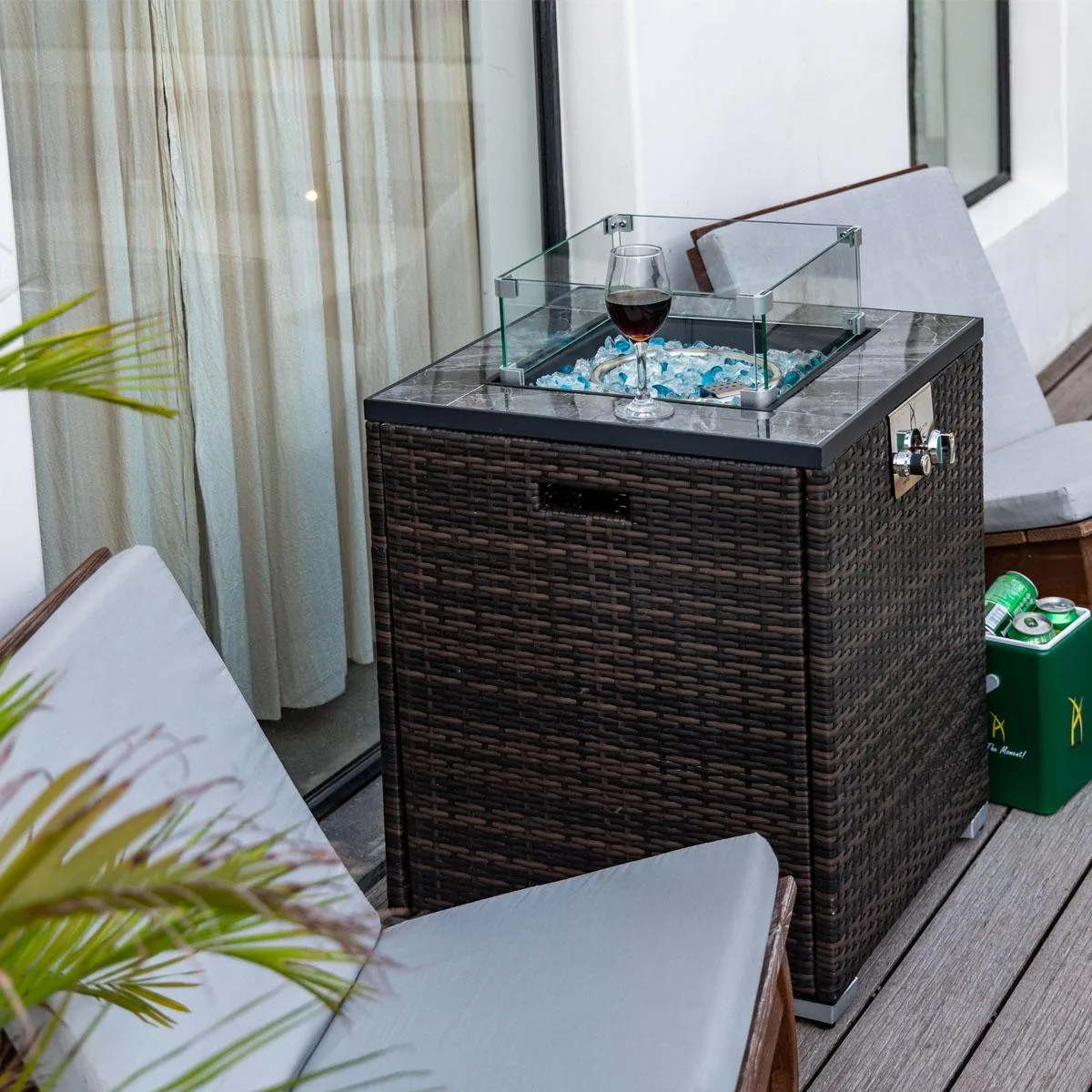 Square propane fire pit table with marble-patterned tile top and espresso wicker base, blue glass beads around burner