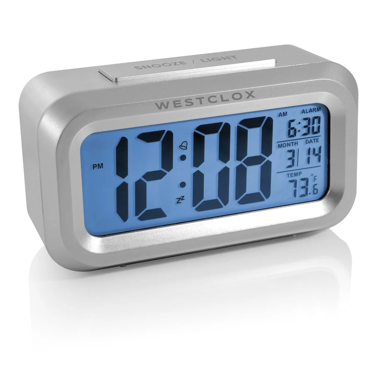 Silver rectangular digital alarm clock with large LCD display, blue backlight button on top, compact 6.1 by 2.2 by 4.7 inch form factor